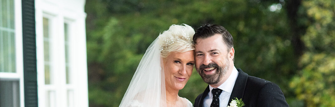 Anne Burrell in a white tulle wedding dress and Stuart Claxton in a classic black tux with orange sneakers on their wedding day in Cazenovia