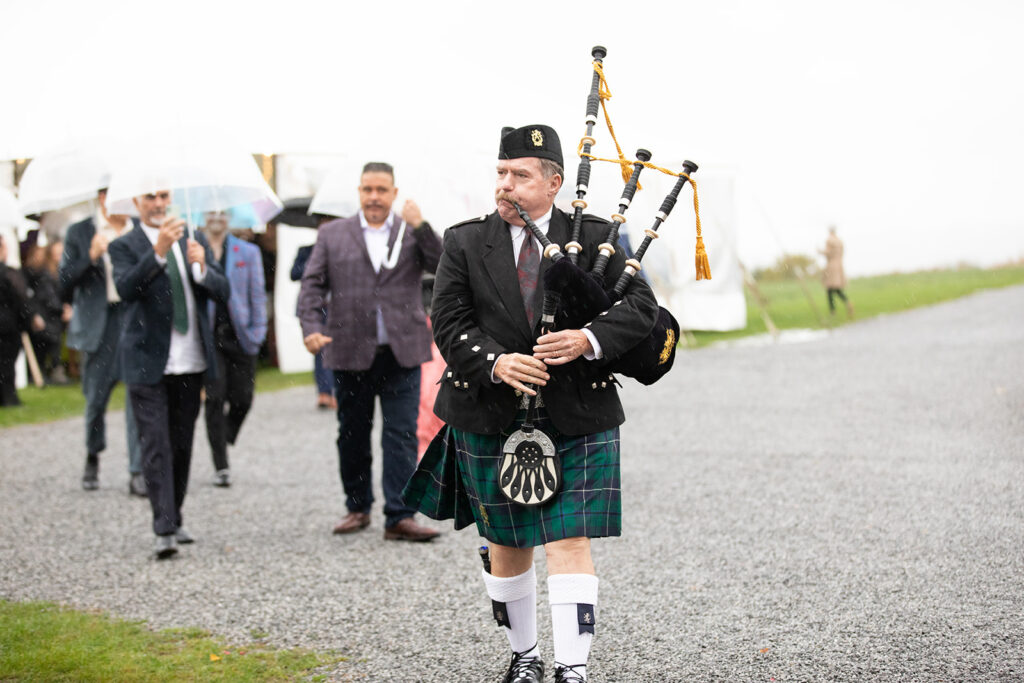 single bagpiper in traditional garb leads wedding guests to cocktail hour