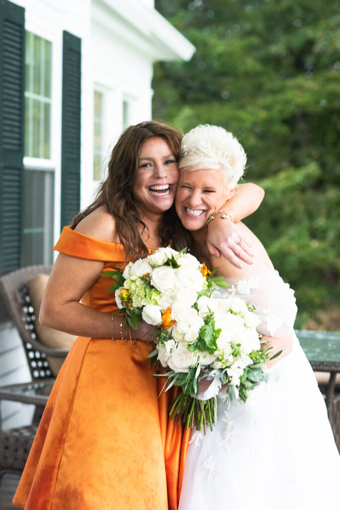 Rachel Ray in orange bridesmaid dress hugs Anne Burrell clutching bouquets 