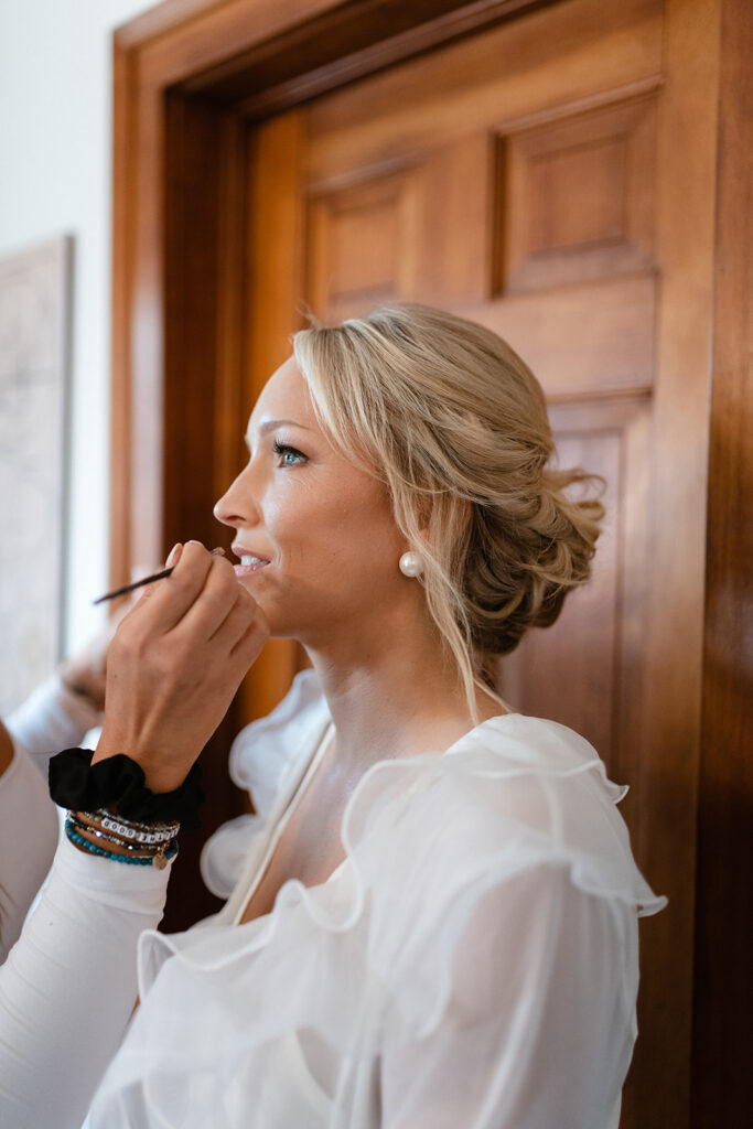 makeup artist applying lipgloss to a bride in a sunlit room at Windridge Estate in Upstate New York