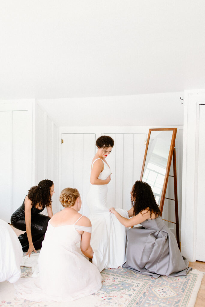 bride standing in front of full length mirror in dress with bridemaids fluffing her