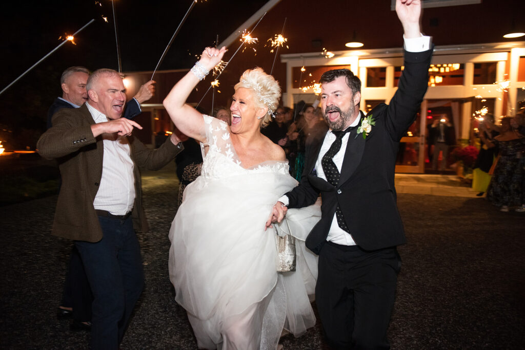 bride and groom racing out of a barn wedding venue with guests creating a sparkler-lit path