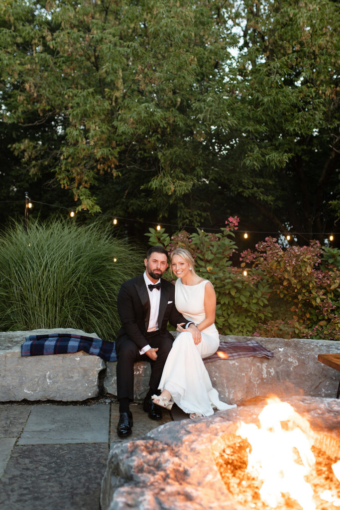 bride and groom sitting at the outdoor stone fire pit in Upstate New York wedding venue 
