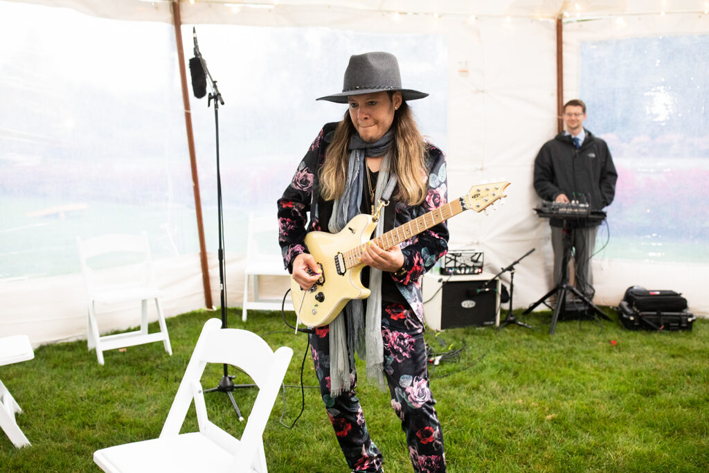 electric guitarist in black fedora and a black and pink floral suit plays at the top of a wedding aisle