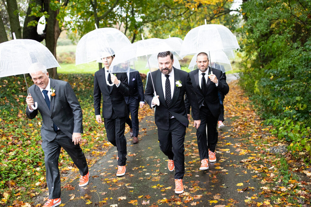 groomsmen walking in black tuxedos with orange Nike sneakers and clear bubble umbrellas