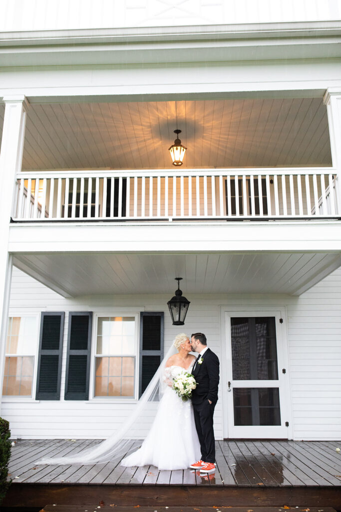 bride and groom kissing under awning of a porch in a historic white estate home