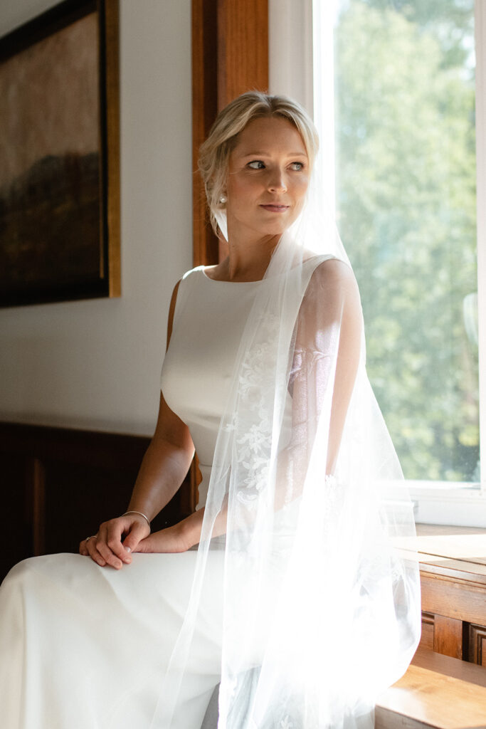 elegant portrait of bride sitting on the edge of a window seat at Windridge estate