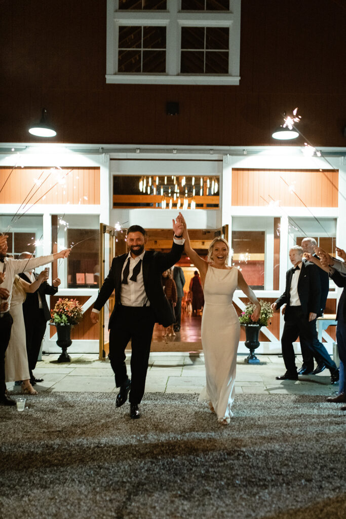 bride and groom exiting red barn wedding venue with sparklers in Upstate New York