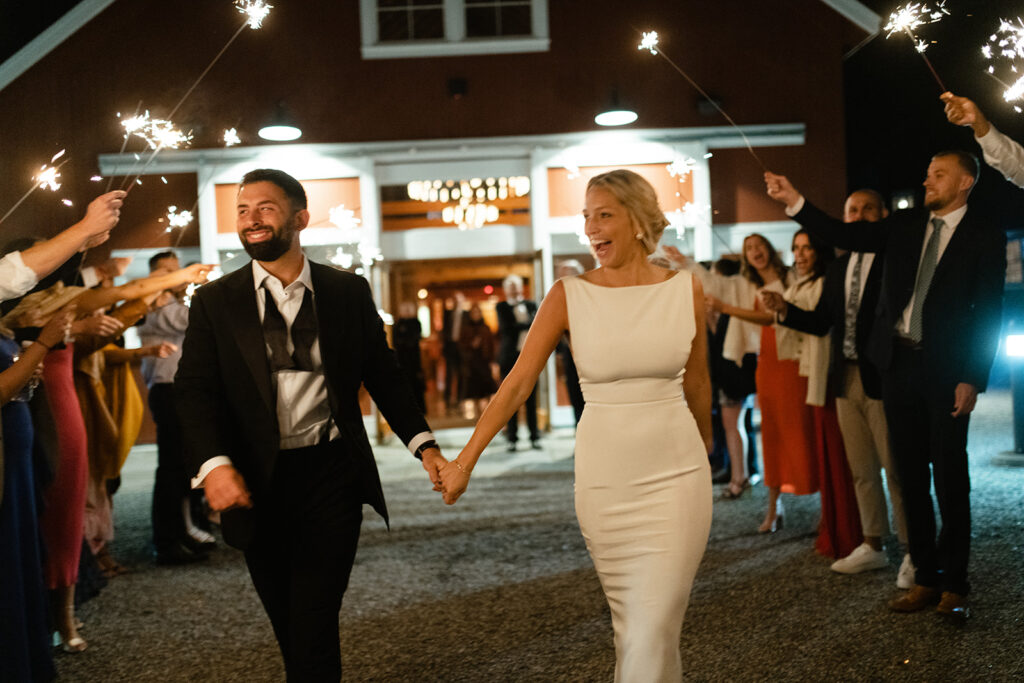 bride and groom exiting red barn wedding venue with sparklers in Upstate New York