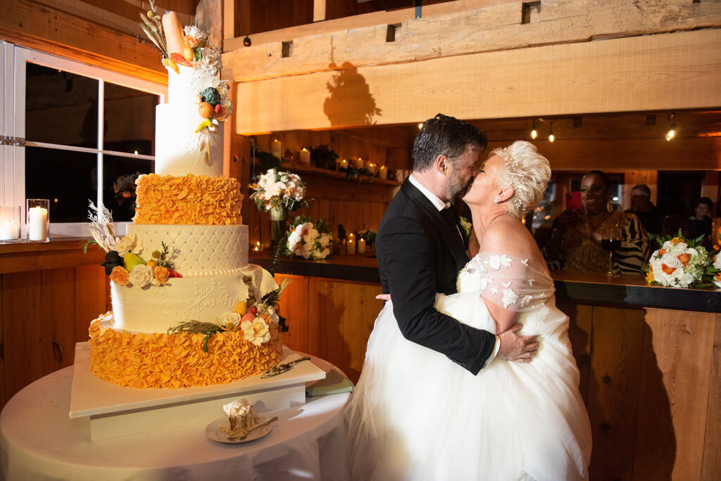 large white and orange piped cake towers with bride and groom kissing in barn upstate