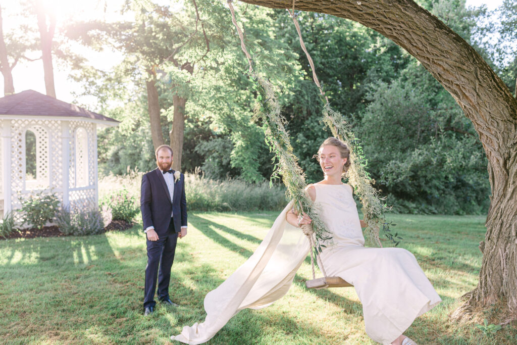 bride in wedding dress swings on nan outdoor tree swing with greenery up the ropes