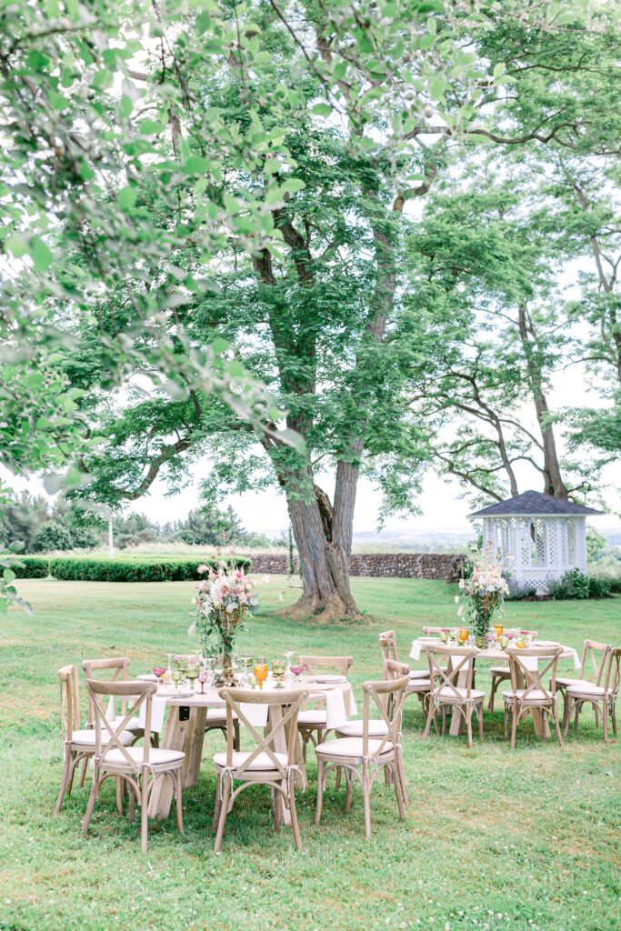 round wood tables decorated and ready for a wedding sit outside under a tree at Windridge Estate 