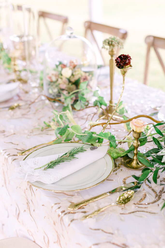 a blush and green floral table includes glass cloches and vintage brass candle holders topped with a floral bud