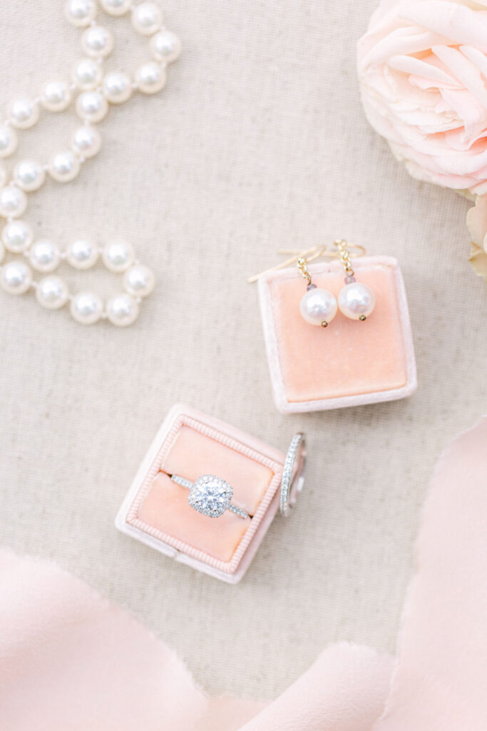 pearl earrings and necklace sit with a white gold diamond ring set alongside blush roses and a velvet box