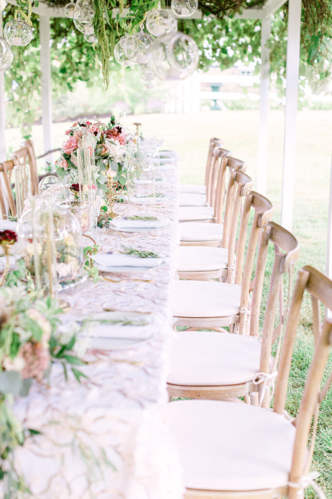 a floral and blush decorated table site under an outdoor pergola covered in grapevines
