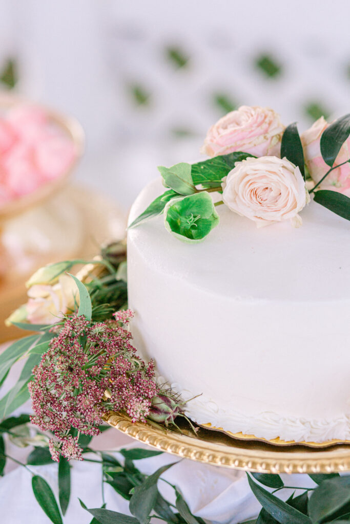 white frosted single-tiered wedding cake with pink blooms and green vines on a vintage gold cake plate