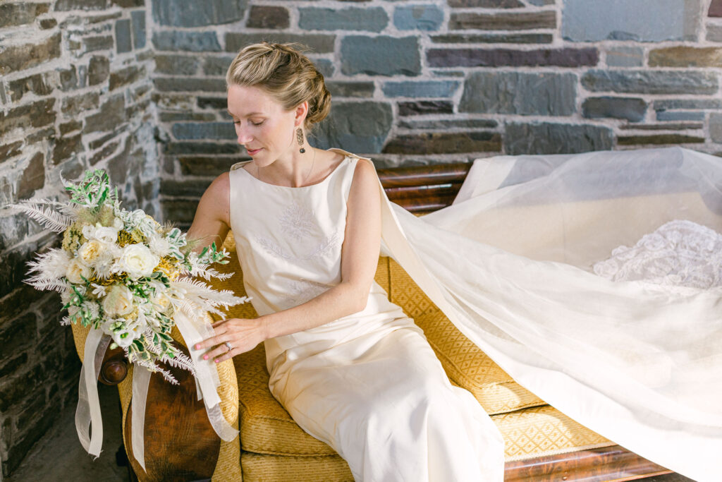 bride in chic, clean lined wedding dress sits admiring her bouquet in a vintage golden settee