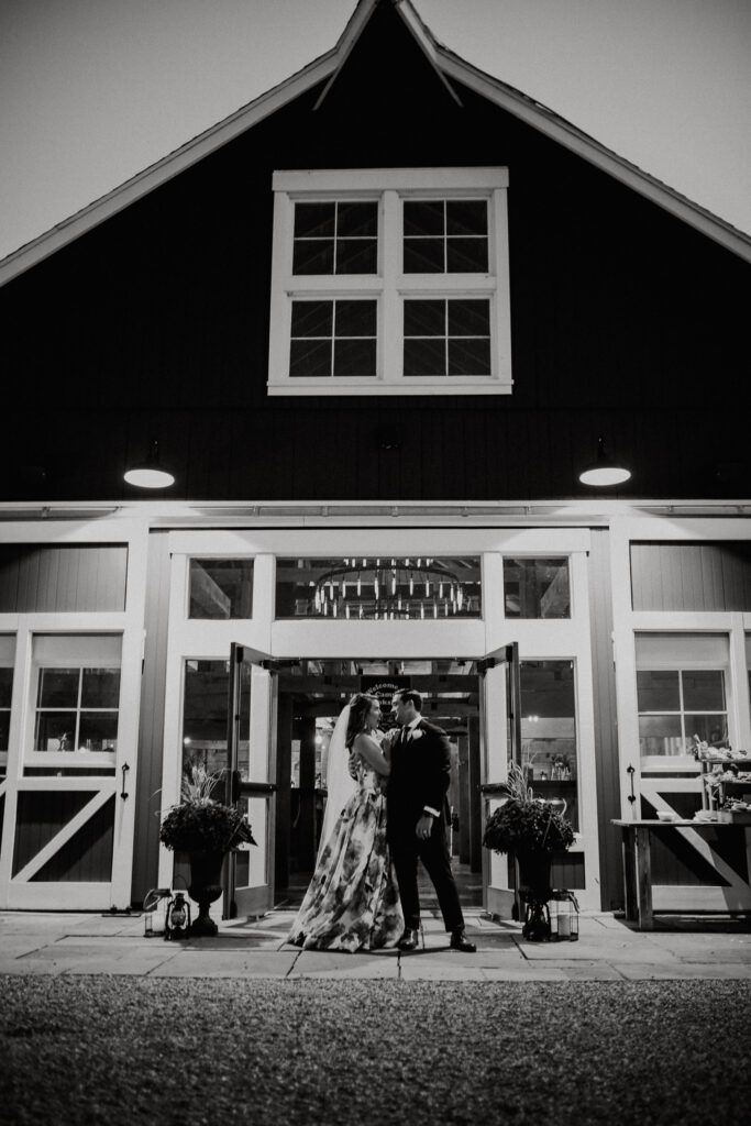 black and white photo of newlyweds in front of a historic barn wedding venue in upstate new york 