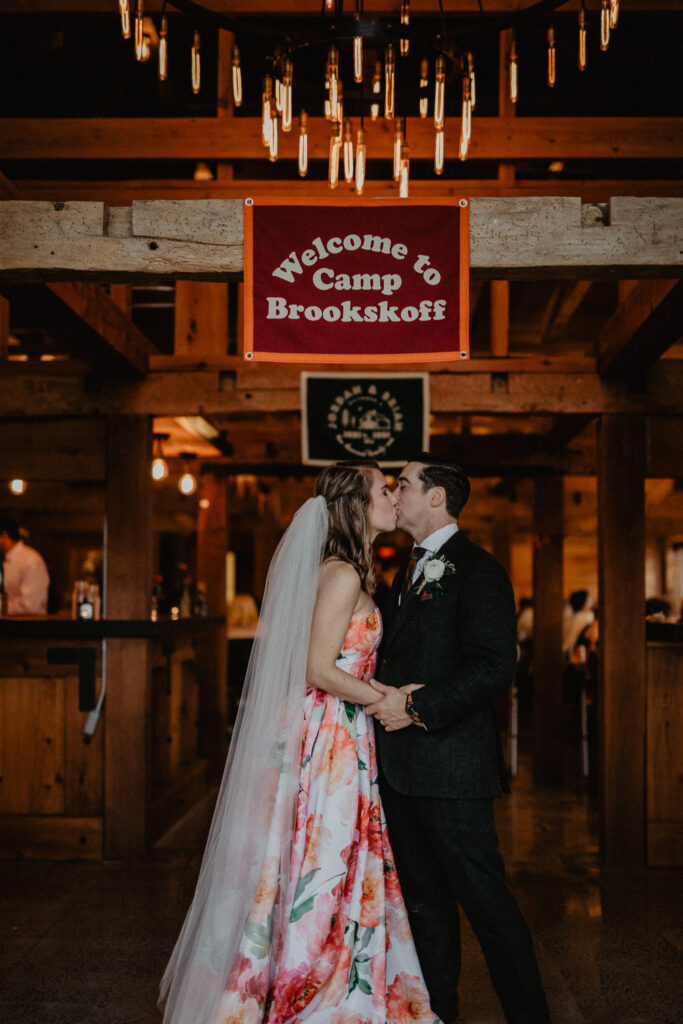 couple kissing under custom oxford pennant for summer camp themed wedding in upstate new york