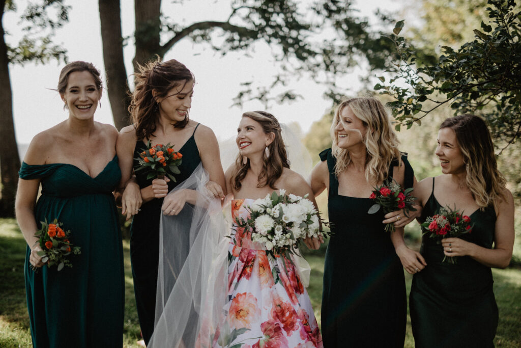 bride in colorful floral wedding dress walks outside with bridesmaids in hunter green dresses 