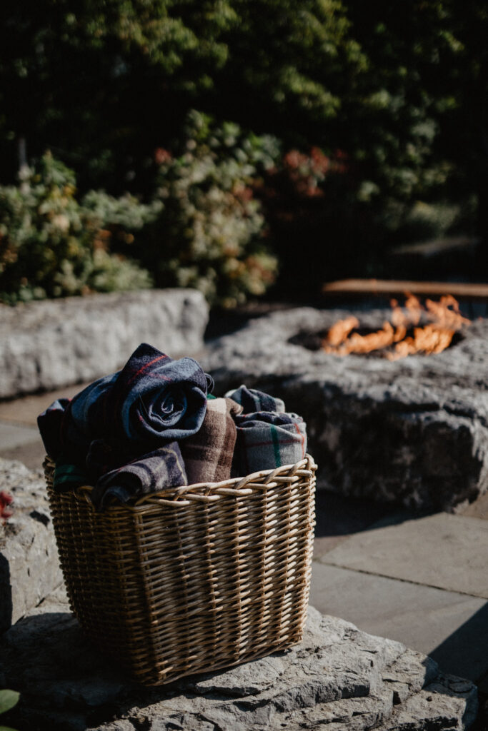 outdoor fire pit with a basket of neatly rolled wool blankets at a wedding venue in upstate new york