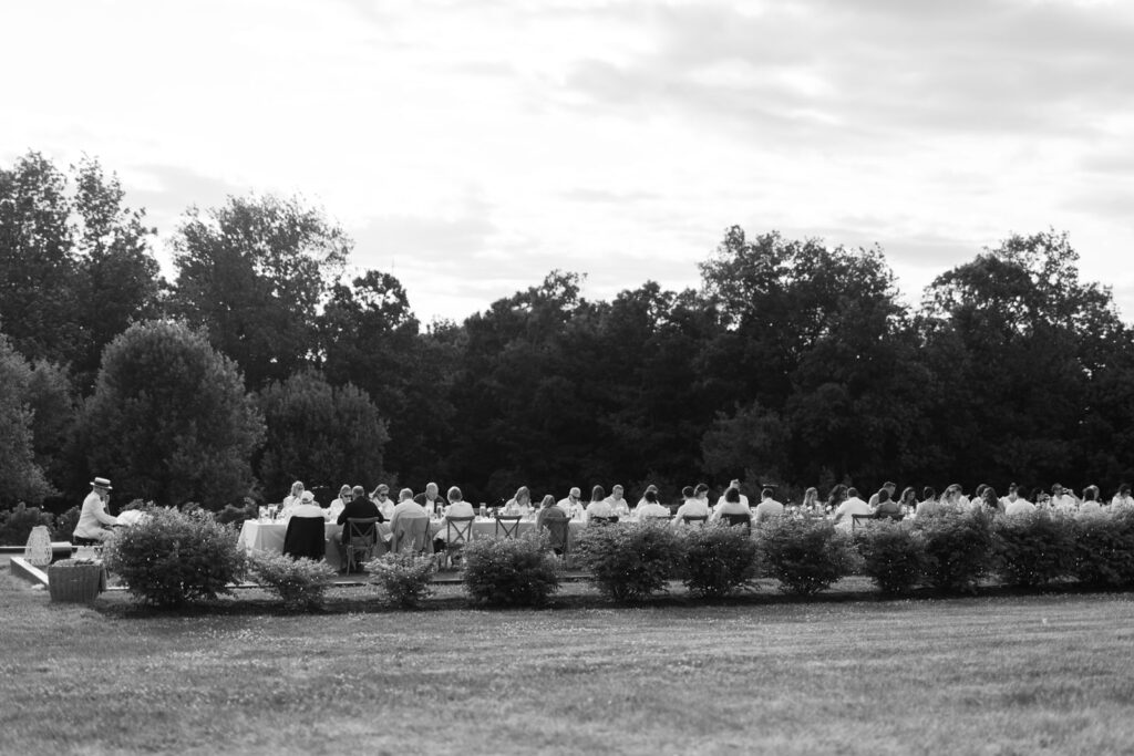 black and white photo of a long table with guests eating outside in upstate new york 