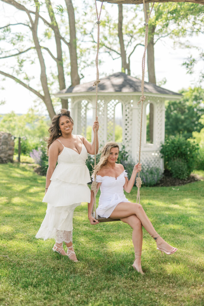 two guests in white dresses on outdoor tree swing in upstate new york